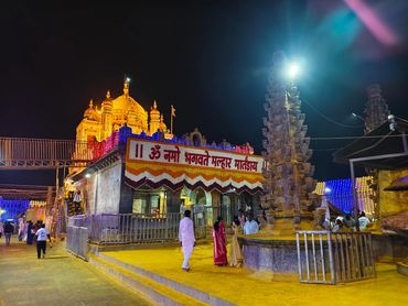 Illuminated Hindu temple at night with visitors in traditional attire.