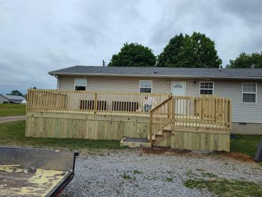 Man sitting on a wooden deck attached to a beige house under a cloudy sky.