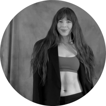 A woman with long hair wearing a blazer and crop top smiling.