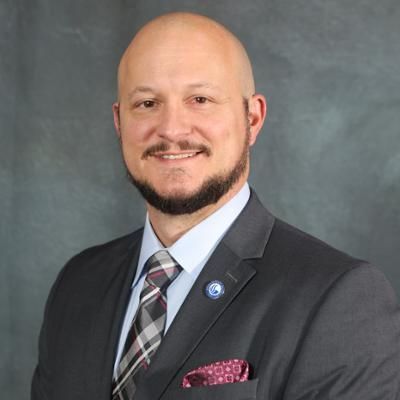 Smiling bald man in suit with patterned tie and pocket square.
