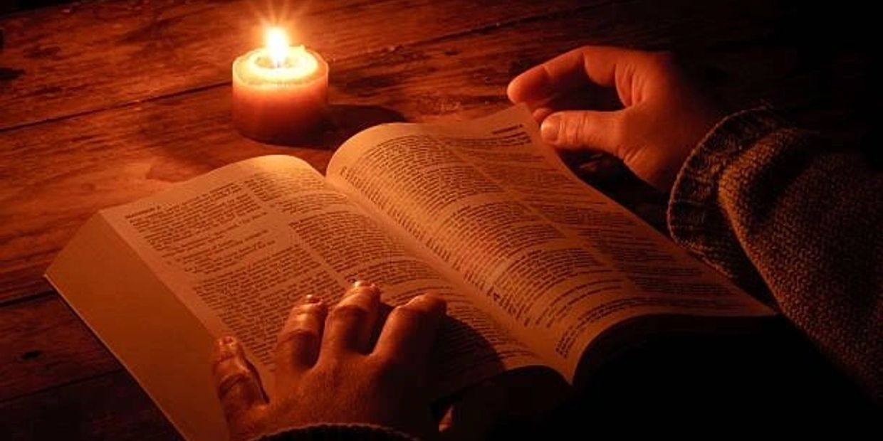 Hands reading a book by candlelight on a wooden table.