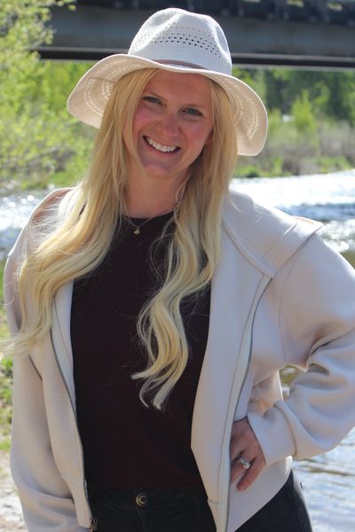Smiling woman outdoors wearing white hat and light jacket.
