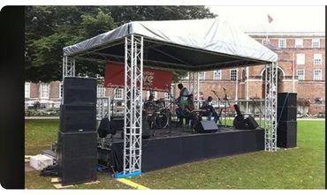 Outdoor stage setup with musicians playing instruments under a canopy.