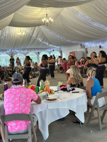 People watch a lively Hawaiian-themed dance performance under a decorated tent.