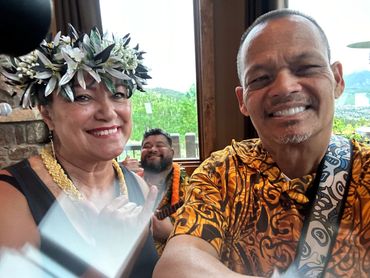 Three people smiling, one wearing a floral headpiece, another playing guitar.