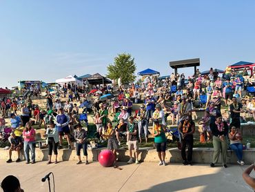 Outdoor cultural event with performers and large audience enjoying under clear skies.
