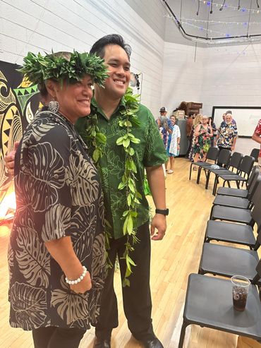 Two people smiling together in traditional Hawaiian attire with leaf leis.