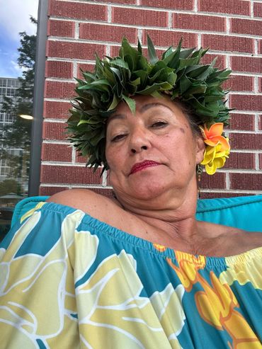 Woman wearing a floral headpiece and colorful off-shoulder dress against a brick wall.