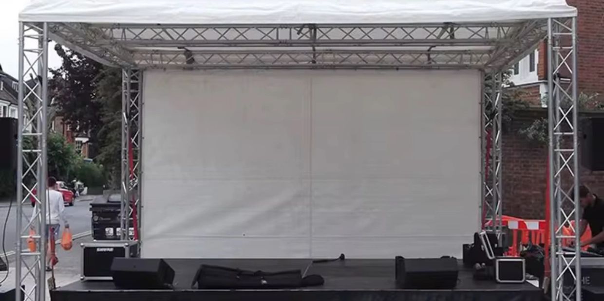 Empty outdoor stage with speakers and equipment under a white canopy.