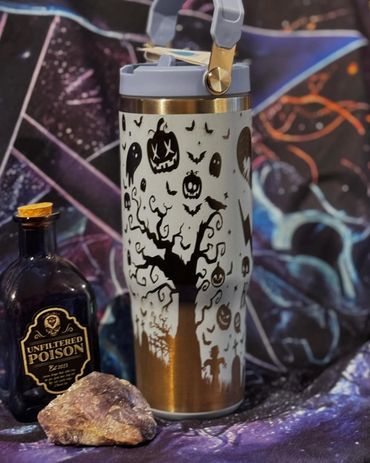 Halloween-themed drink tumbler with spooky designs and a bottle labeled 'Unfiltered Poison' beside a crystal.