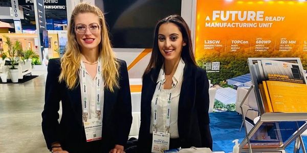 Two professionally dressed female PTM event staff at a colorful manufacturing trade show booth