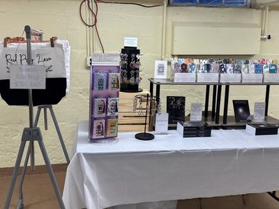 Table display with books, jewelry, and a sign for bracelets and tote bags.