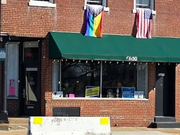 Brick storefront with green awning, displaying pride and American flags.