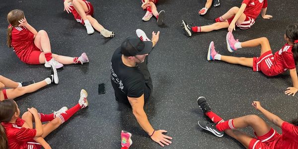 Coach stretching with young soccer players in a circle.