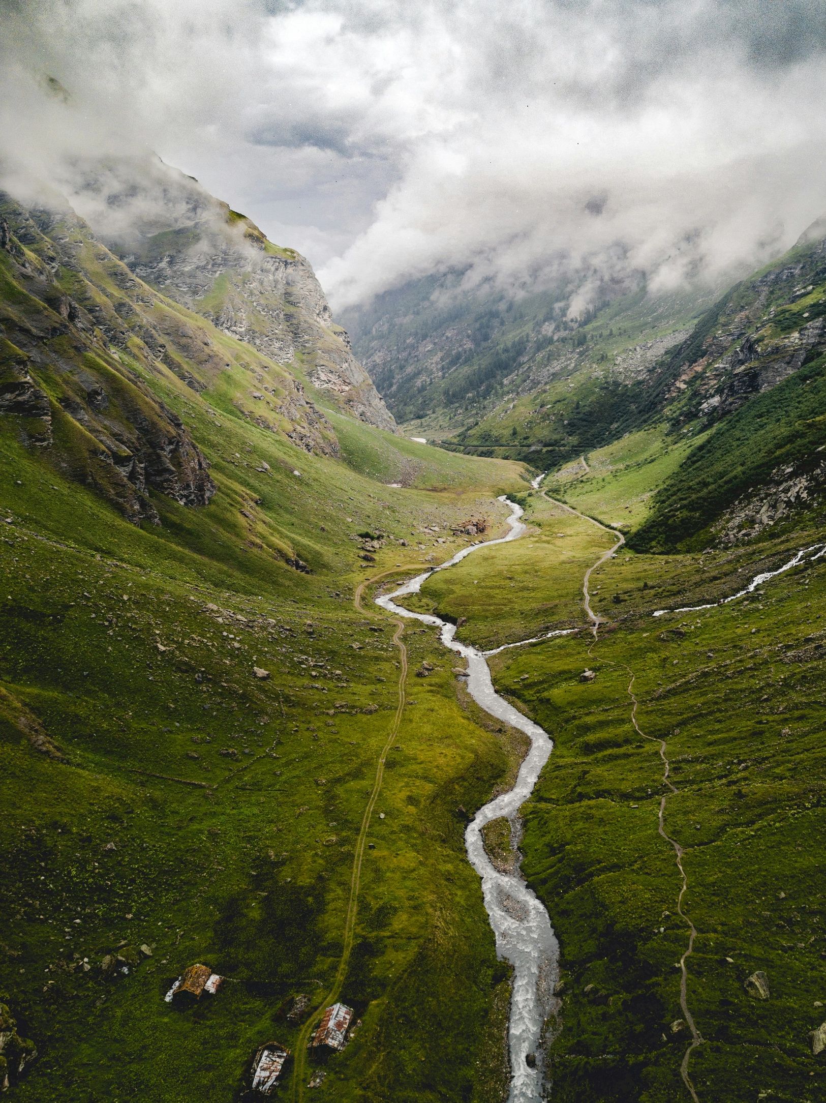 A winding river flows through a lush green valley surrounded by misty mountains.