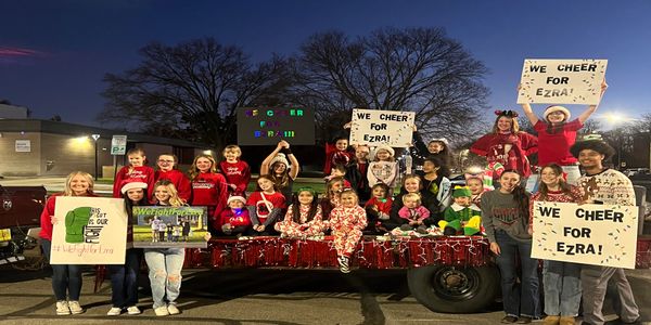 Group of people holding signs cheering for Ezra at night outdoors.