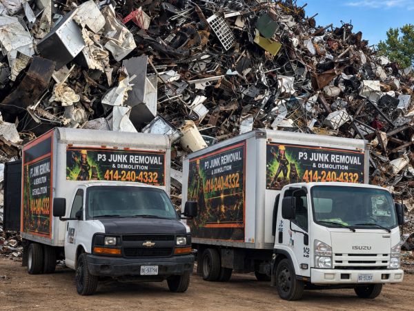Two junk removal trucks parked in front of a large scrap pile. psjunkremovalwi