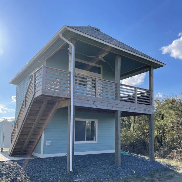 Small blue two-story house with wooden stairs and balcony under a clear sky.