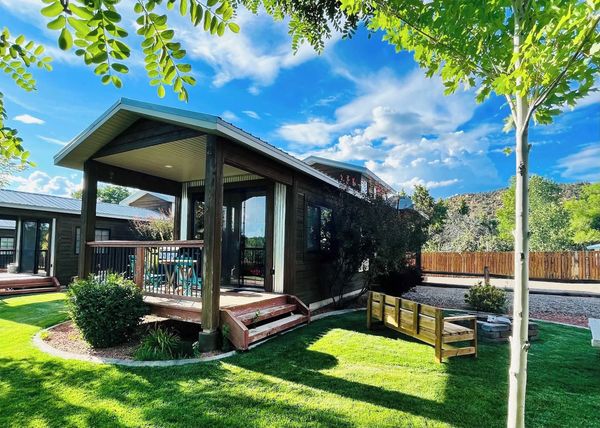 A cozy cabin with a porch surrounded by green grass and trees under a blue sky.