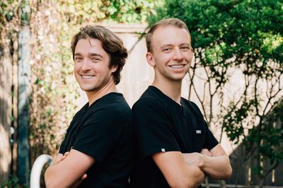 Two men standing back to back smiling outdoors.