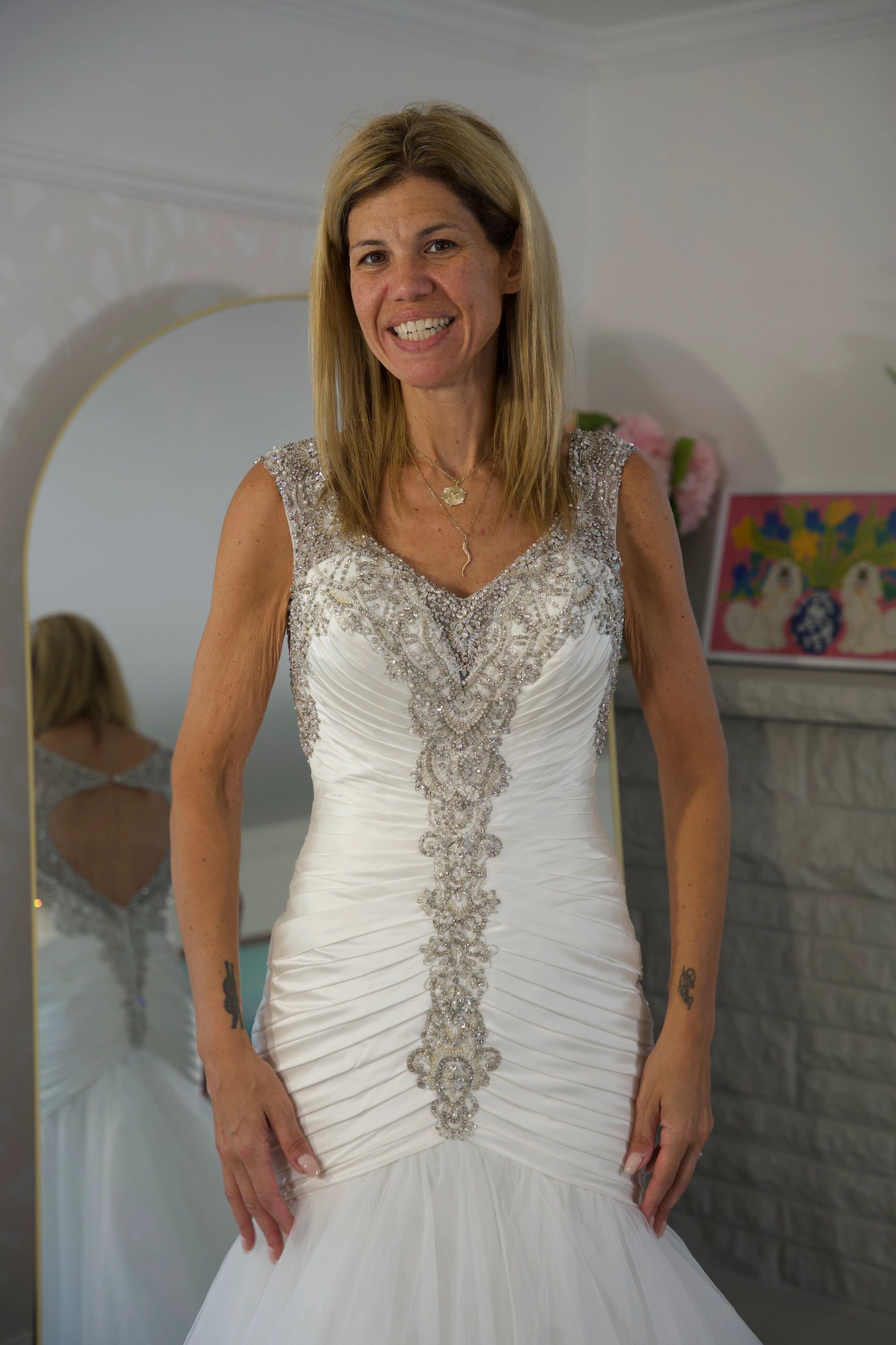 Woman smiling in an elegant white dress with silver embellishments.