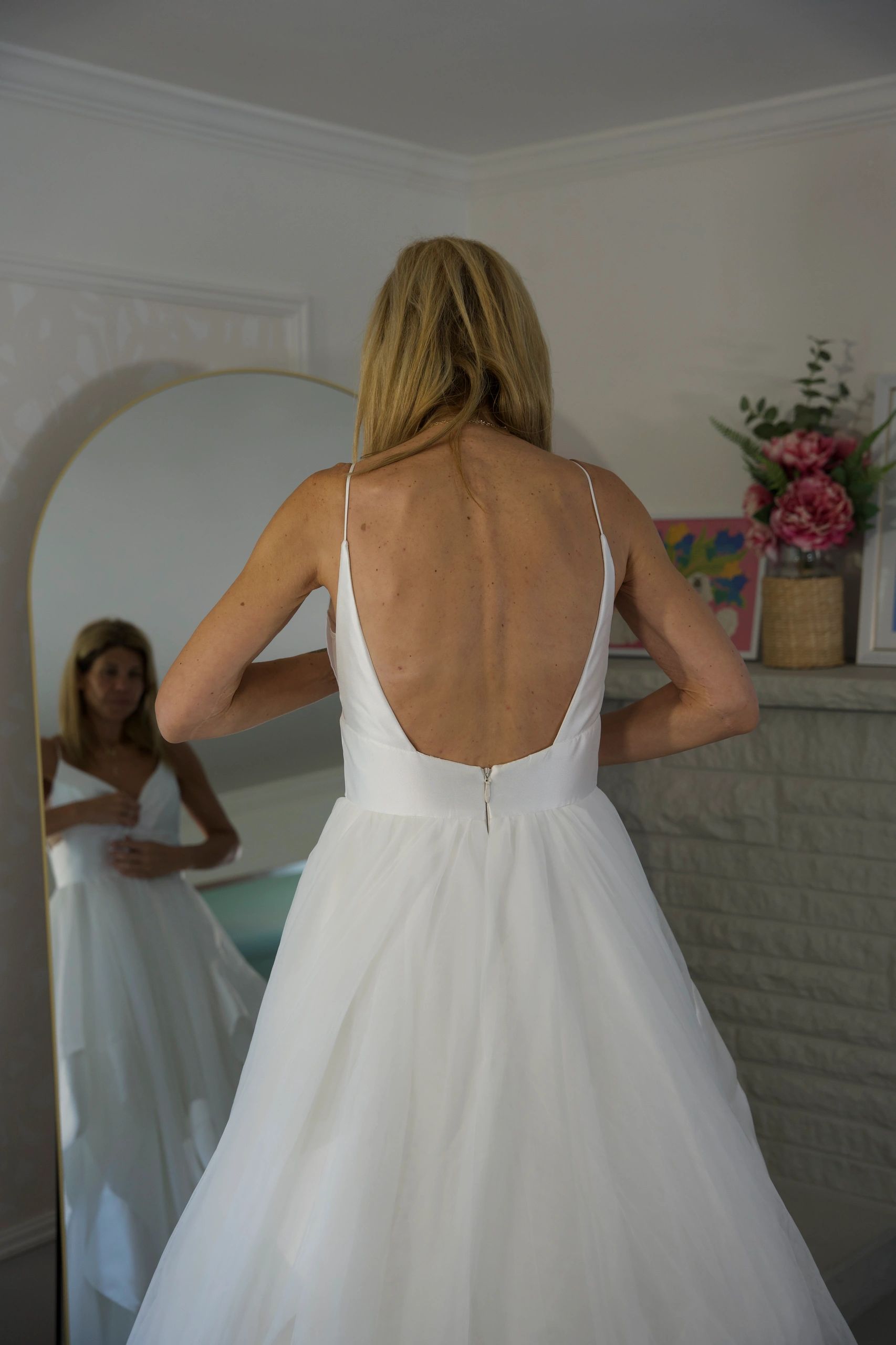Woman in white dress looking in mirror.
