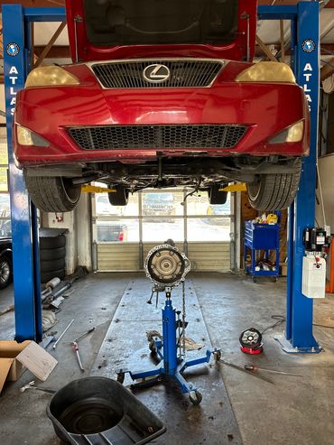 Red Lexus car on lift with removed transmission in a garage.