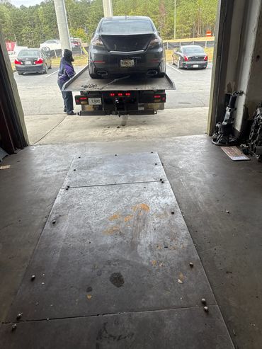 A black car is being loaded onto a tow truck inside a garage.