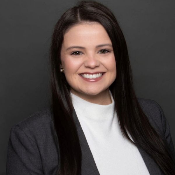 Professional portrait of a smiling woman in business attire against a gray background.