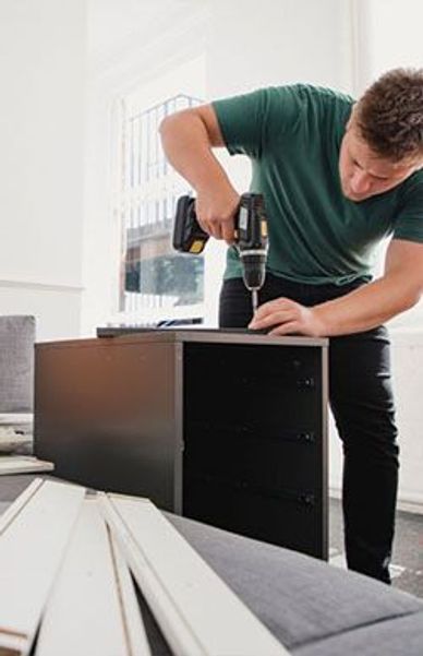 A man assembling furniture using a power drill indoors.