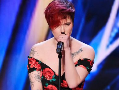 Aubrey Burchell Singing into a microphone a black dress with red roses and a blue background