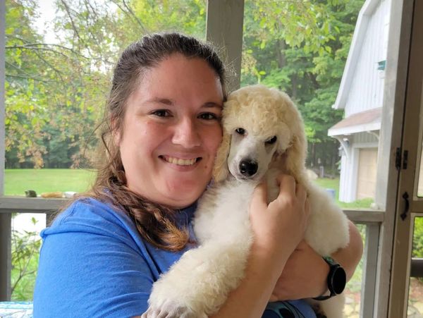 Woman smiling and holding a white poodle puppy.
