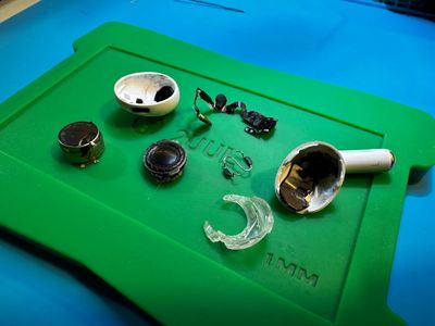 Disassembled wireless earbud components on a green mat.