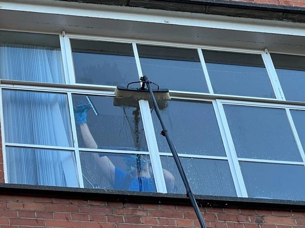 Person cleaning large windows with a squeegee and brush on an extension pole.