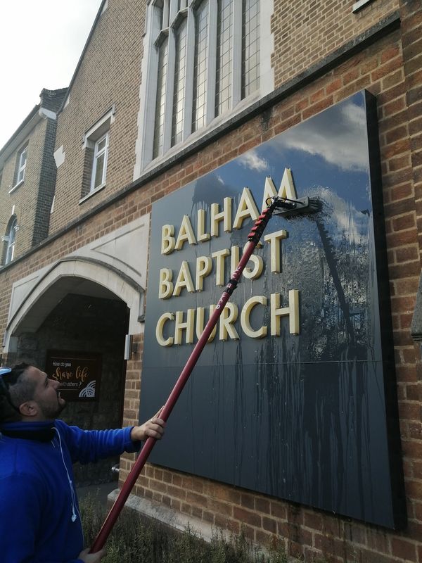 A man cleaning the Balham Baptist Church sign with a long brush.