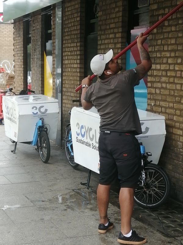 A man holding a red pole near branded cargo bikes on a city sidewalk.