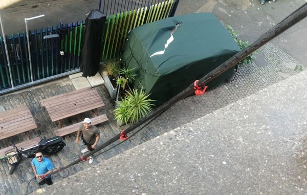 Two men look up from a cobblestone courtyard with picnic tables and plants.