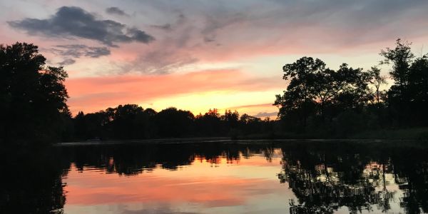 A tranquil sunset reflecting on a calm lake surrounded by trees.
