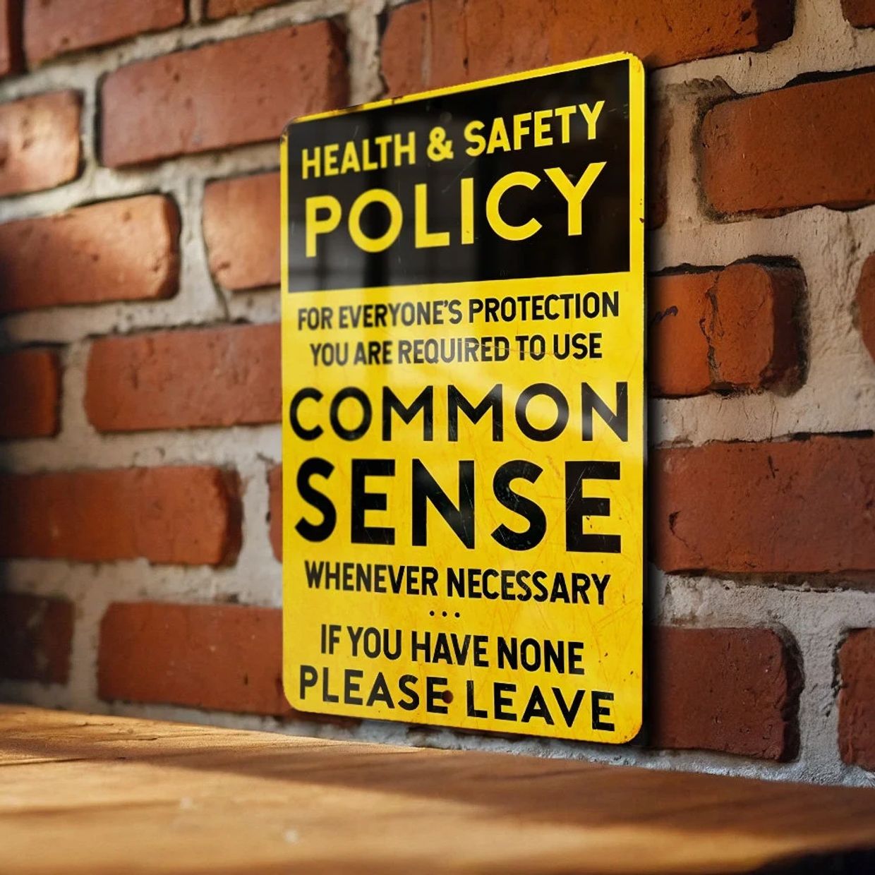 Yellow health and safety sign on a brick wall about using common sense.