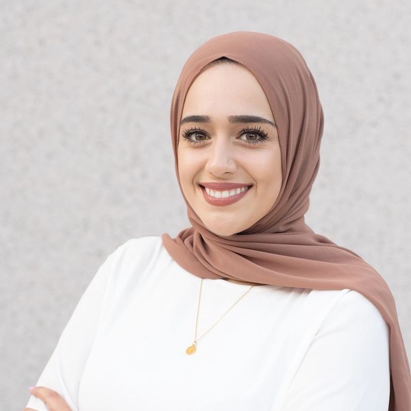 Smiling woman wearing a brown hijab and white top.