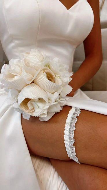 Bride in a white dress holding a bouquet, showing a lace garter on her thigh.