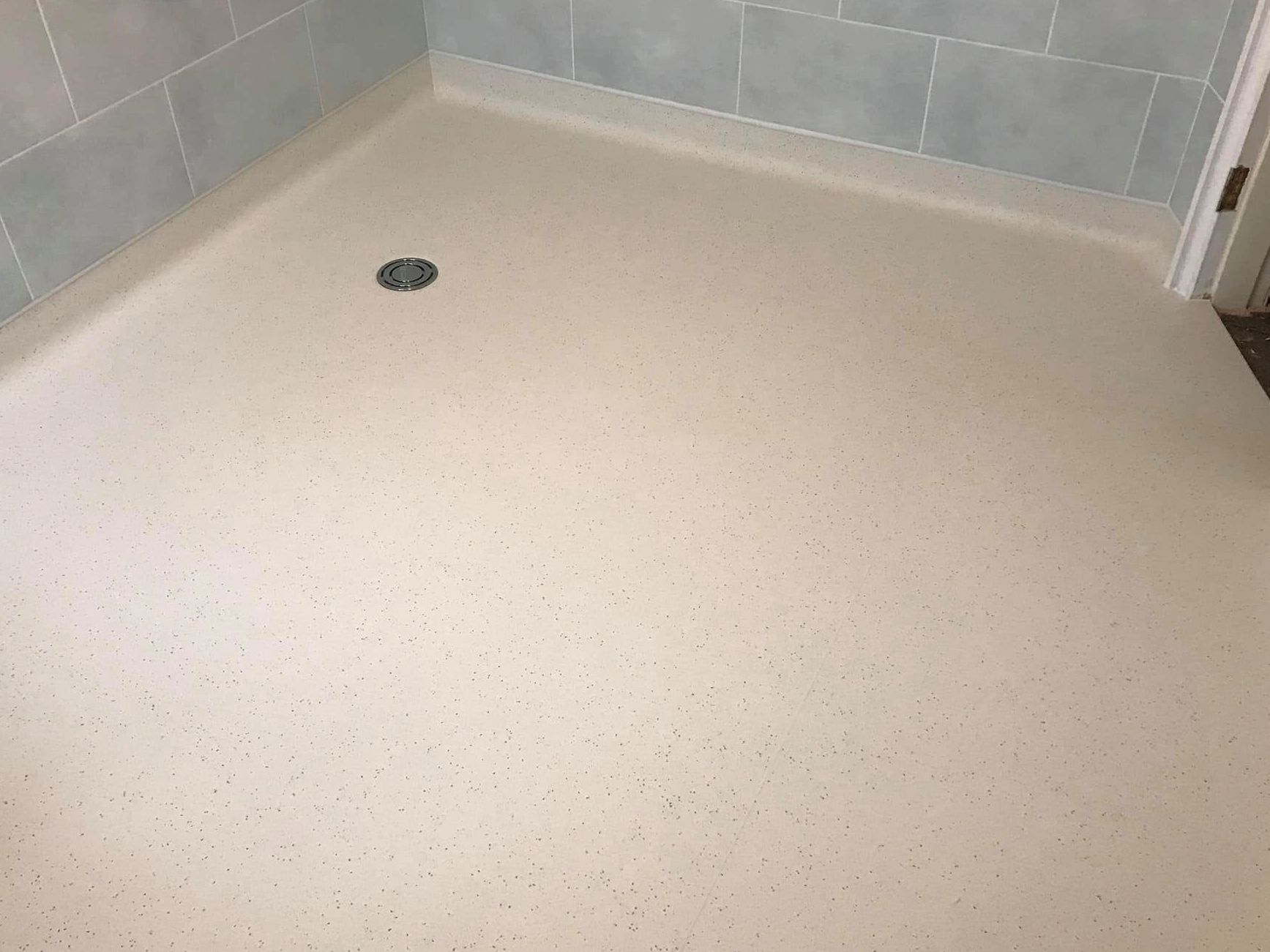Newly installed beige shower floor with drain and light blue tiled walls.
