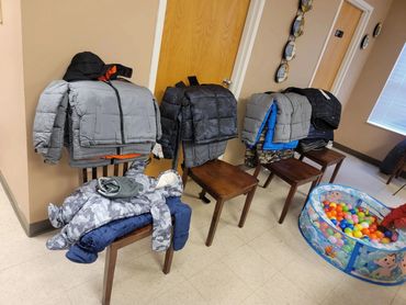 Multiple winter jackets folded and placed on wooden chairs indoors.