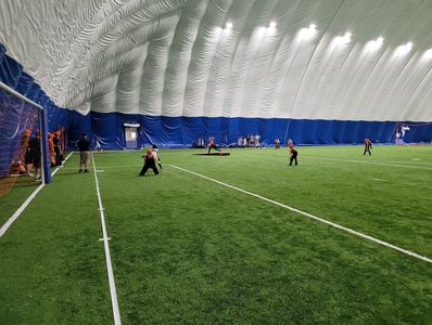 Children playing soccer inside a large indoor dome with artificial turf.