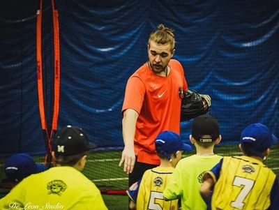 Coach instructing young baseball players during practice indoors.