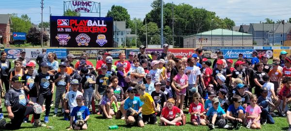 Large group of children and adults at a baseball event on a sunny day.