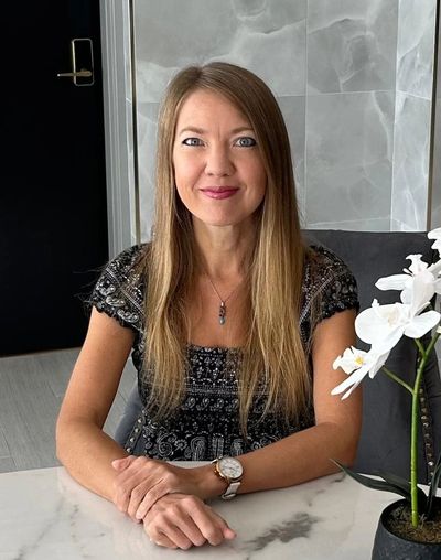 Smiling woman with long hair sitting at a table with a white orchid beside her.