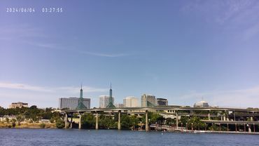 Cityscape with modern buildings and a bridge over a river under clear blue sky.