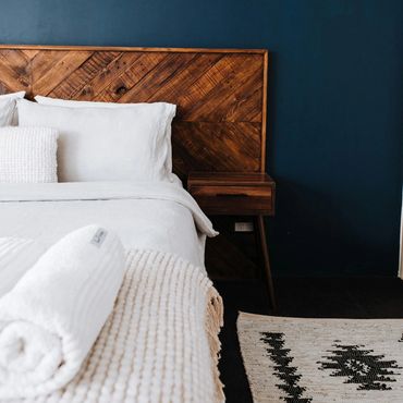 bed with wood headboard, white linens and dark wall