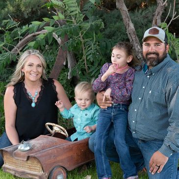 A happy family with two children posing outdoors with a vintage toy car.